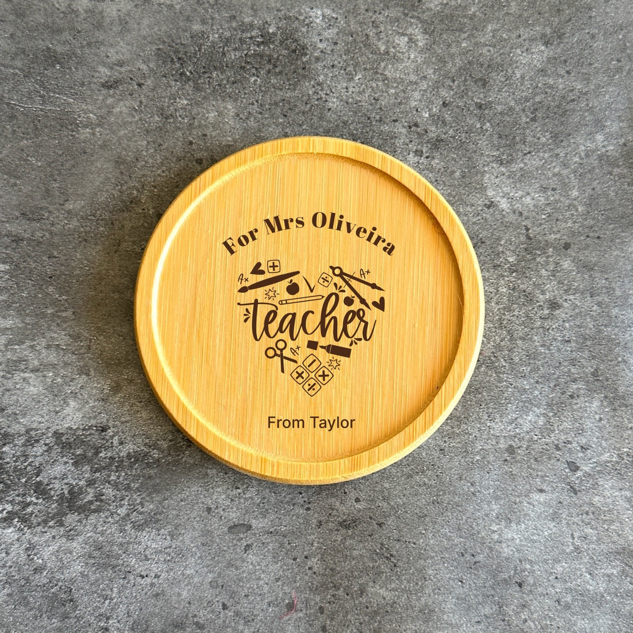 A wooden coaster with a personalized message engraved on it, sitting on a gray surface.