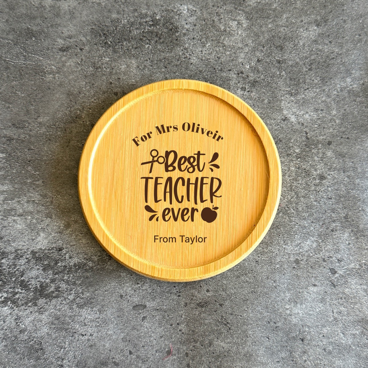 A wooden coaster with a personalized message engraved on it, placed on a gray surface.