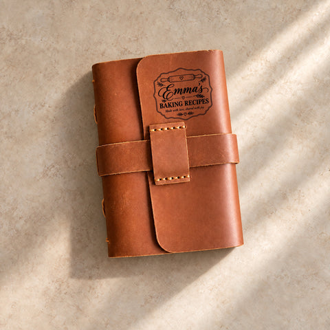  Personalised leather recipe journal with strap closure engraved with a mixing bowl, whisk, flowers and the words A little flour. A lot of love.