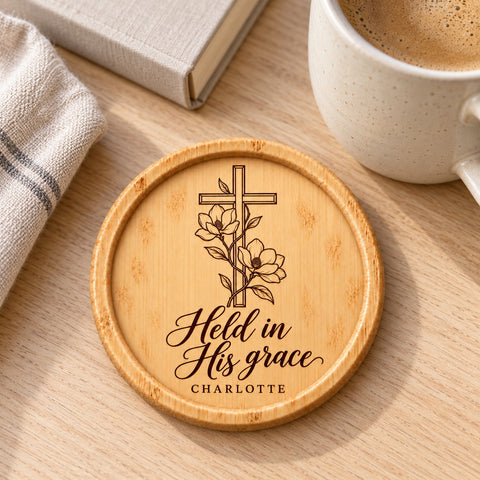 Christian wooden coaster with a floral cross and Held in His grace engraving.
